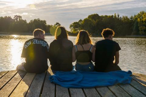 Fire unge sidder sammen på en badebro ved en sø